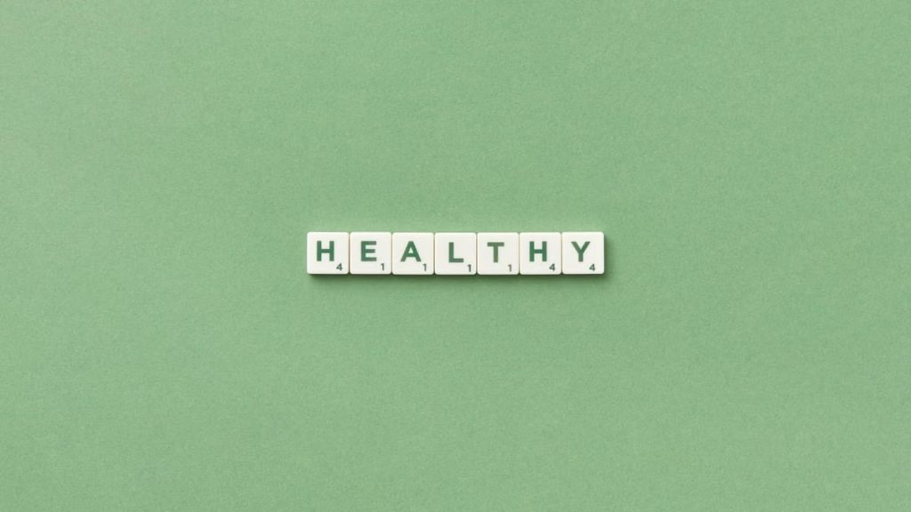 Scrabble tiles spelling the word 'healthy' on a light green background, top view.