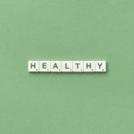 Scrabble tiles spelling the word 'healthy' on a light green background, top view.
