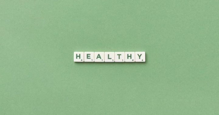 Scrabble tiles spelling the word 'healthy' on a light green background, top view.